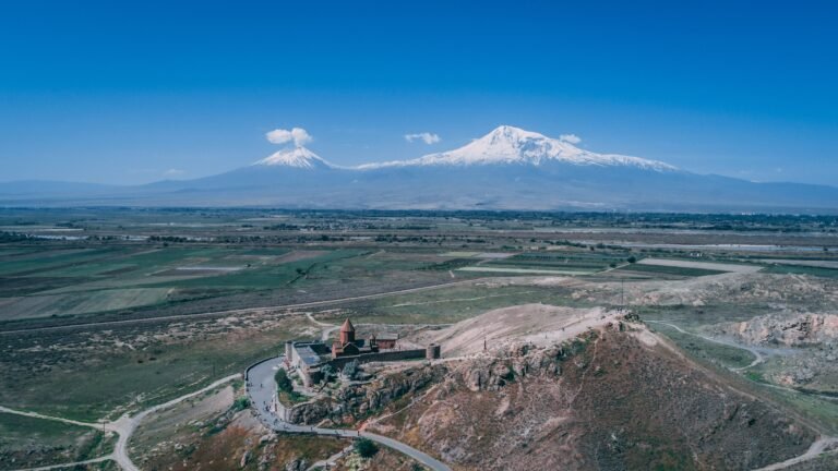 Aerial shot of an Armenian church on a hill with Mount Ararat and a clear blue sky